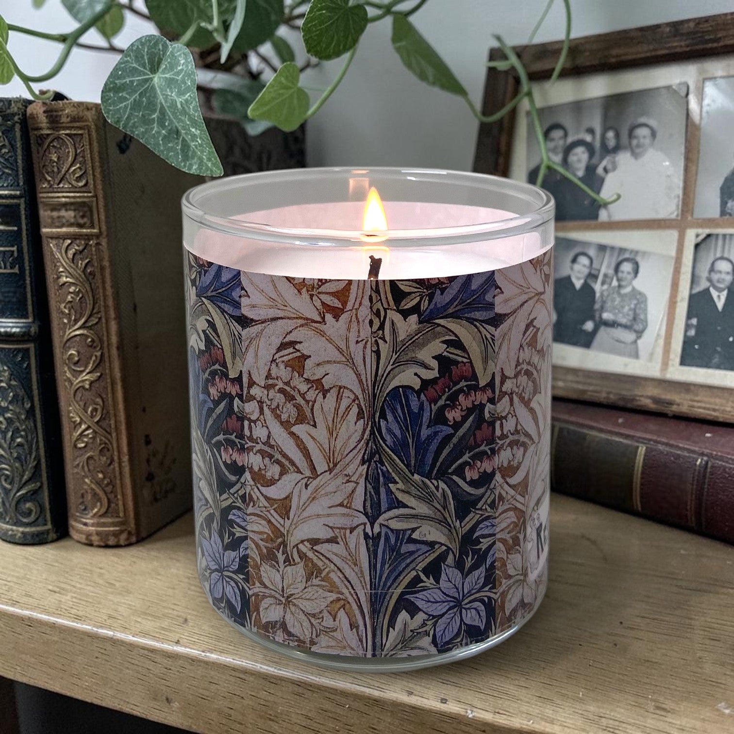 Candle with floral and Acanthus leaf pattern on a wooden surface next to books and family photos
