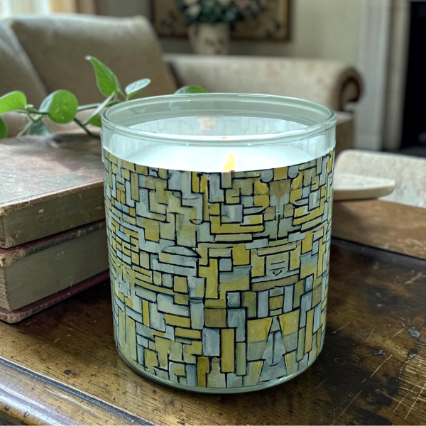 Candle in a patterned jar on a wooden table with a living room background