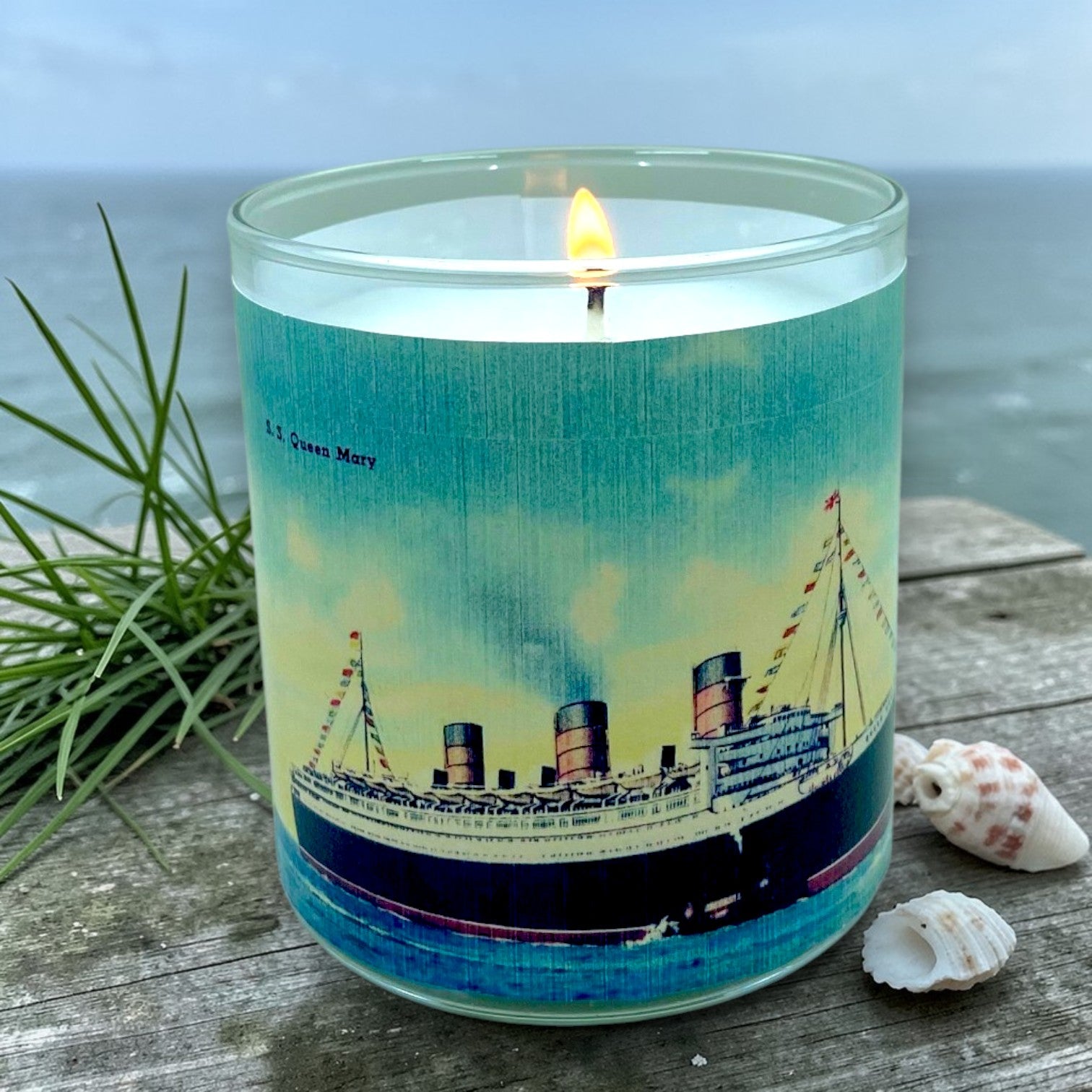 Candle with a ship design on a wooden surface near water
