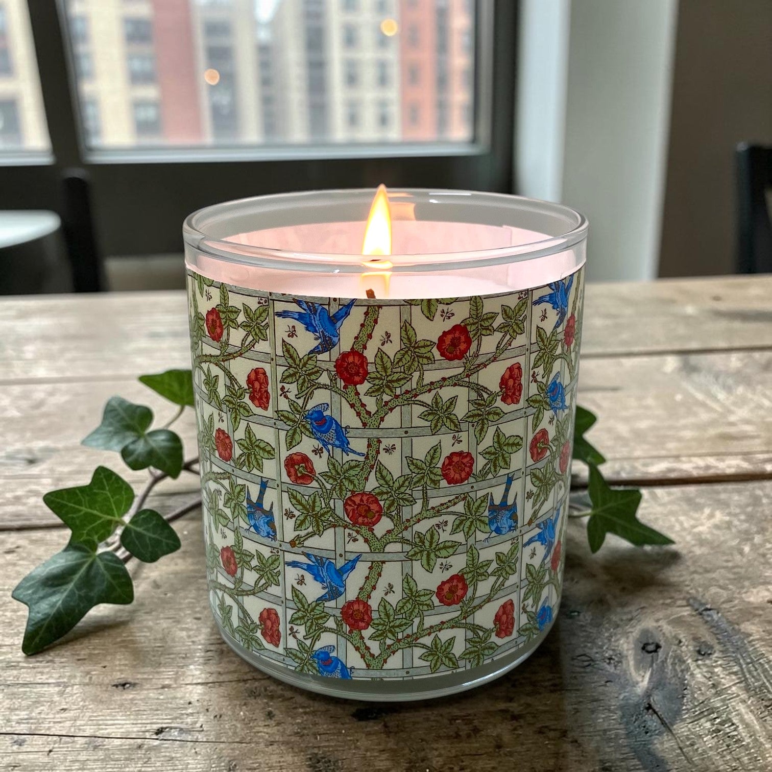 Candle in a decorative glass jar with floral pattern on a wooden surface.