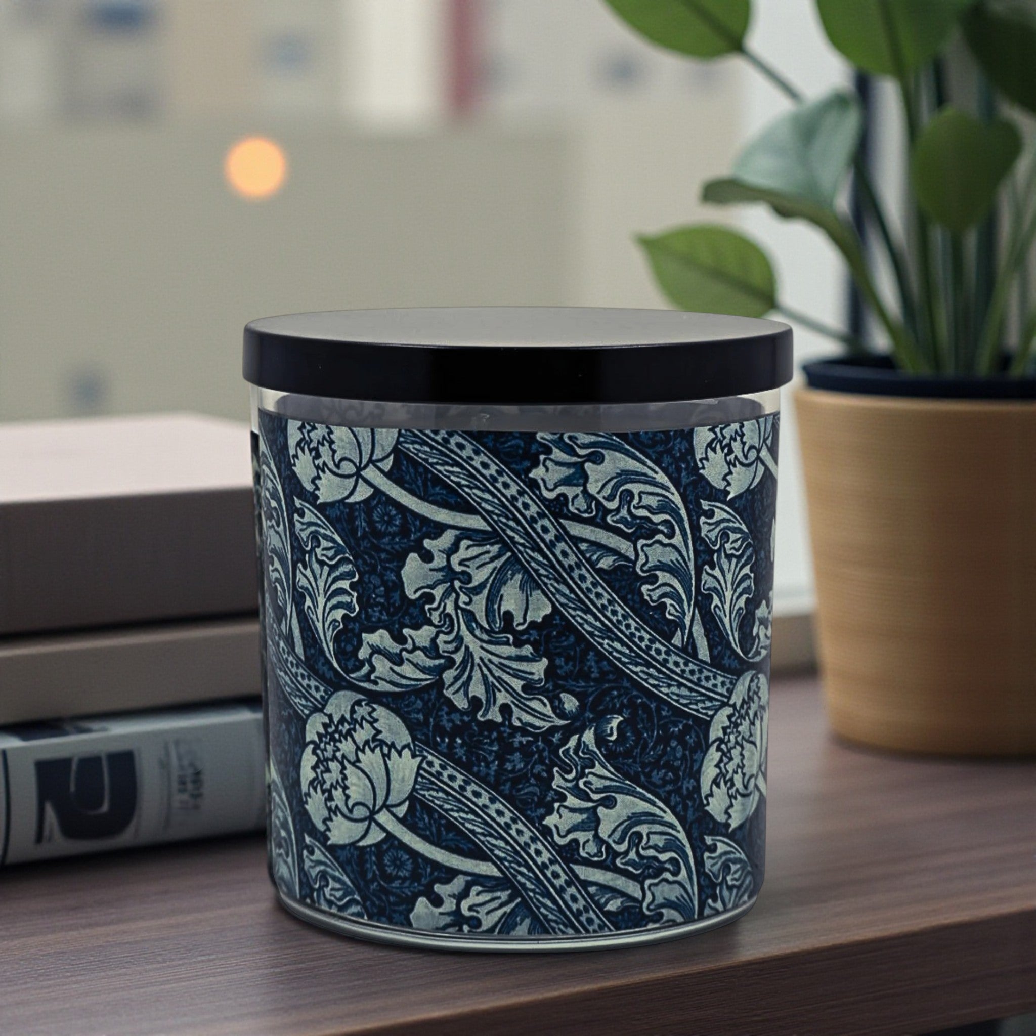 Decorative candle with paisley pattern on a table next to books and a plant
