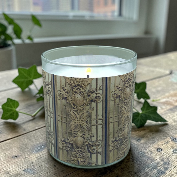 Decorative candle with intricate patterns on a wooden surface with green leaves.
