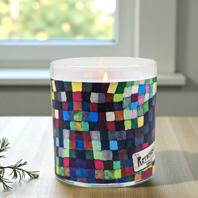 Candle with colorful checkered design on a table near a window