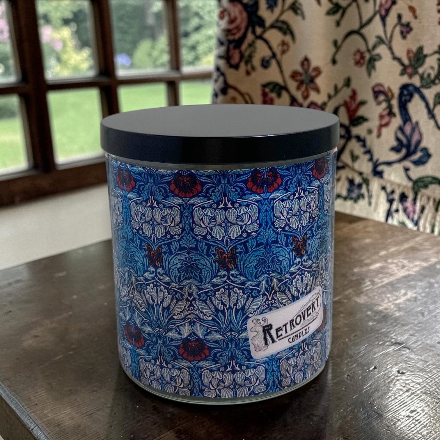 Candle in a decorative container with a floral pattern on a wooden surface.