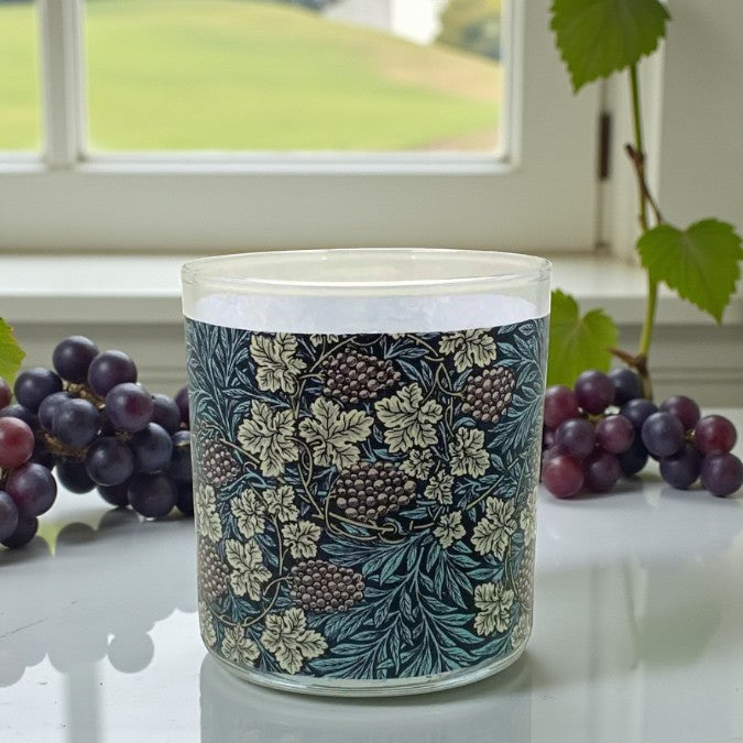 Decorative candle with floral pattern in front of a window with grapes on a windowsill.