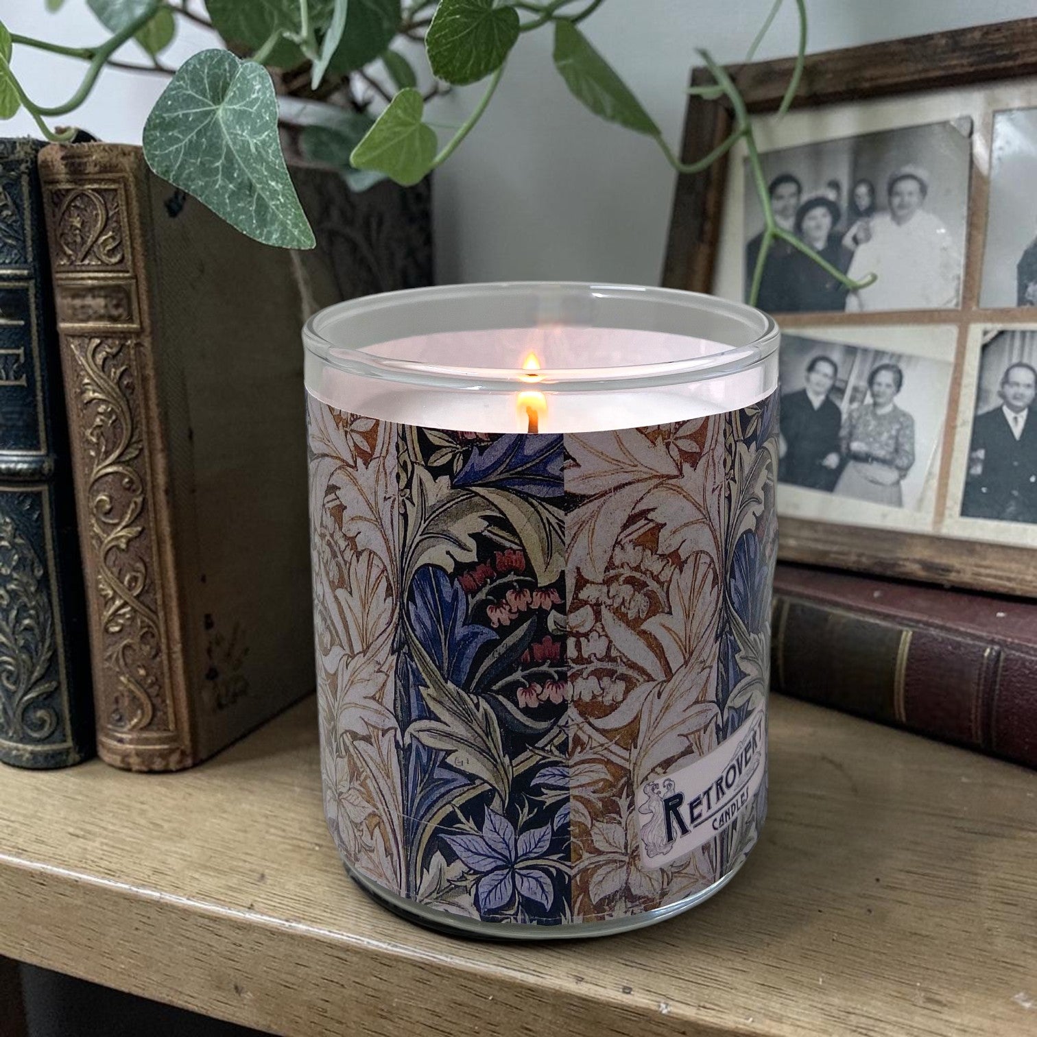 Candle with floral and acanthus William Morris design on a wooden surface with books and family photos in the background