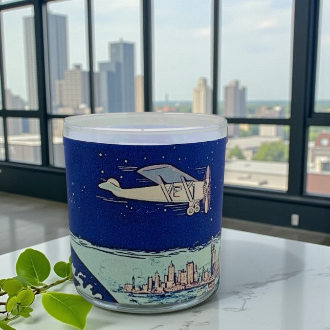 Cylindrical container with airplane design on a cityscape background, placed on a surface with a window view in the background.