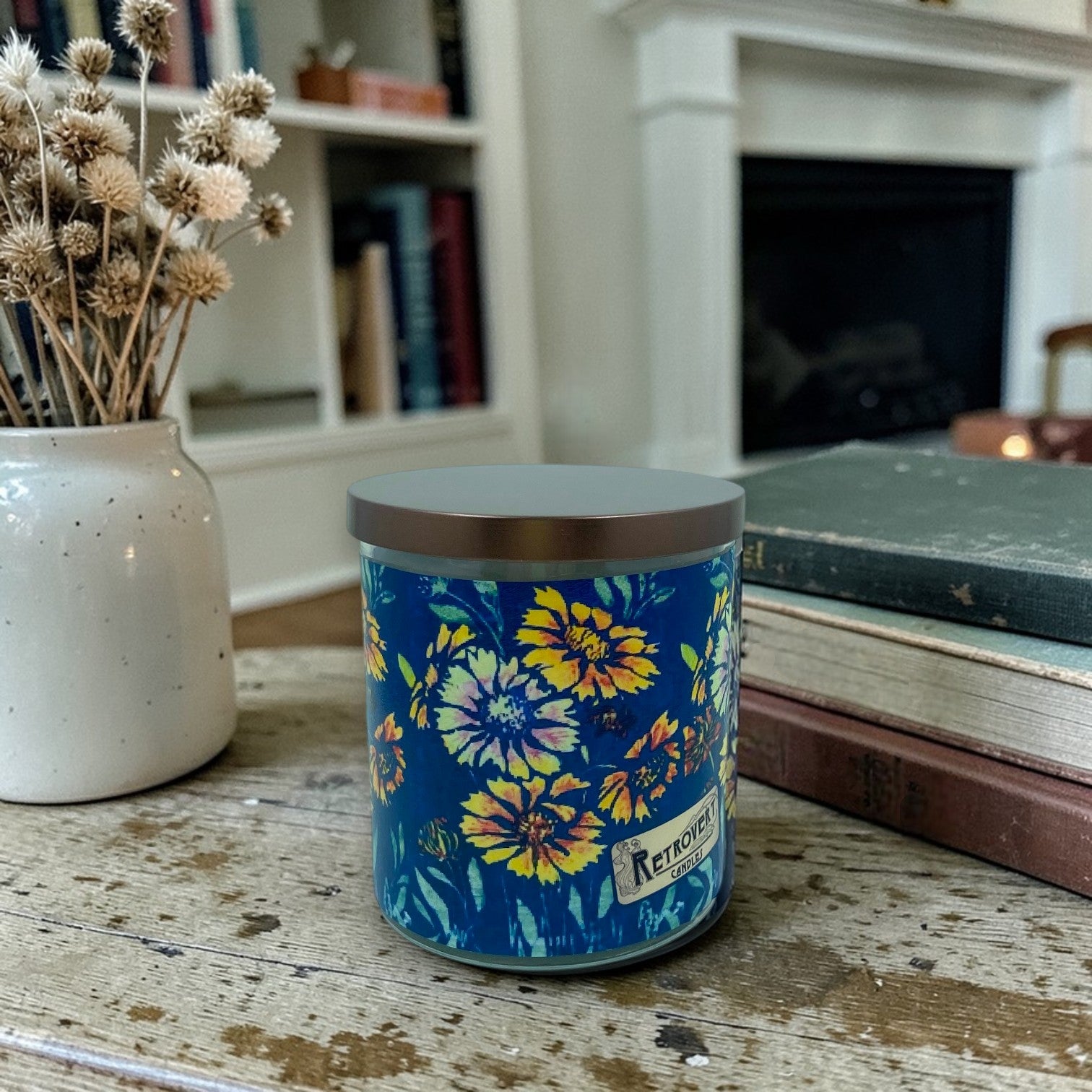 Candle with Frances Gearhart Arts & Crafts era woodblock print floral design on a wooden surface, with a vase of dried flowers and books in the background.