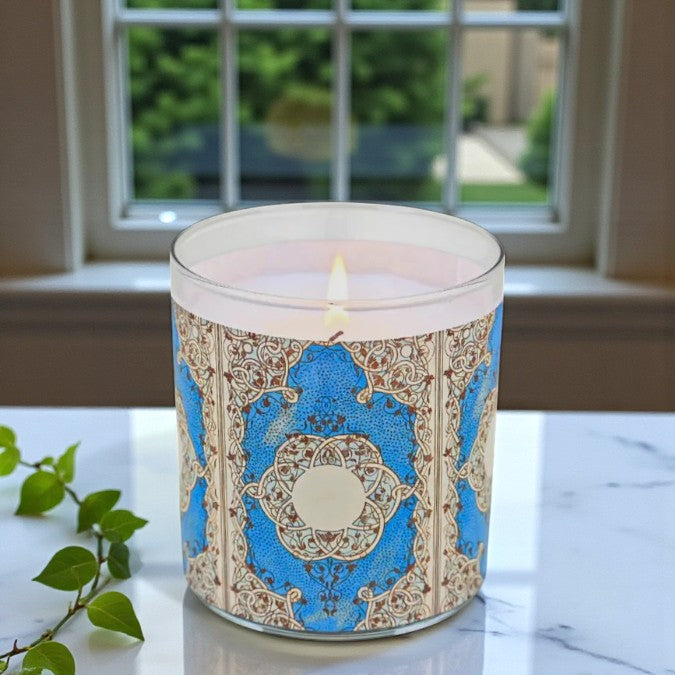 Decorative candle with a blue and gold pattern on a marble surface with a window in the background.