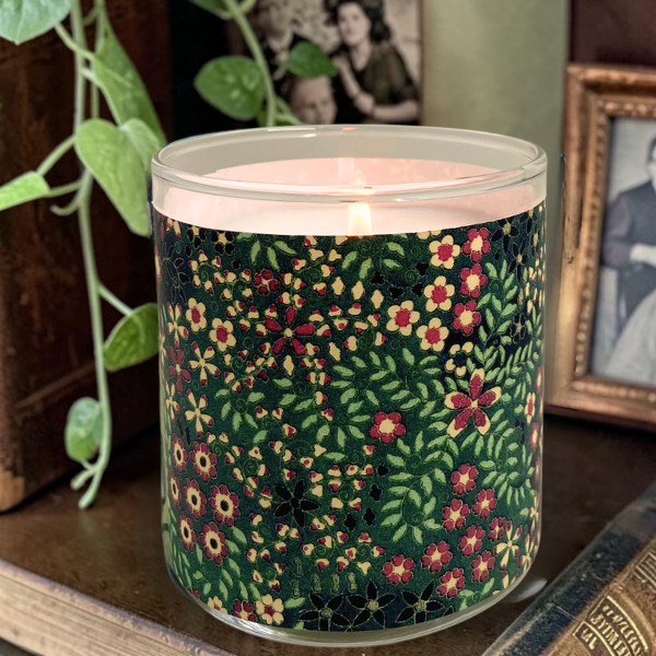 Candle with floral pattern on a surface with photos and plants in the background