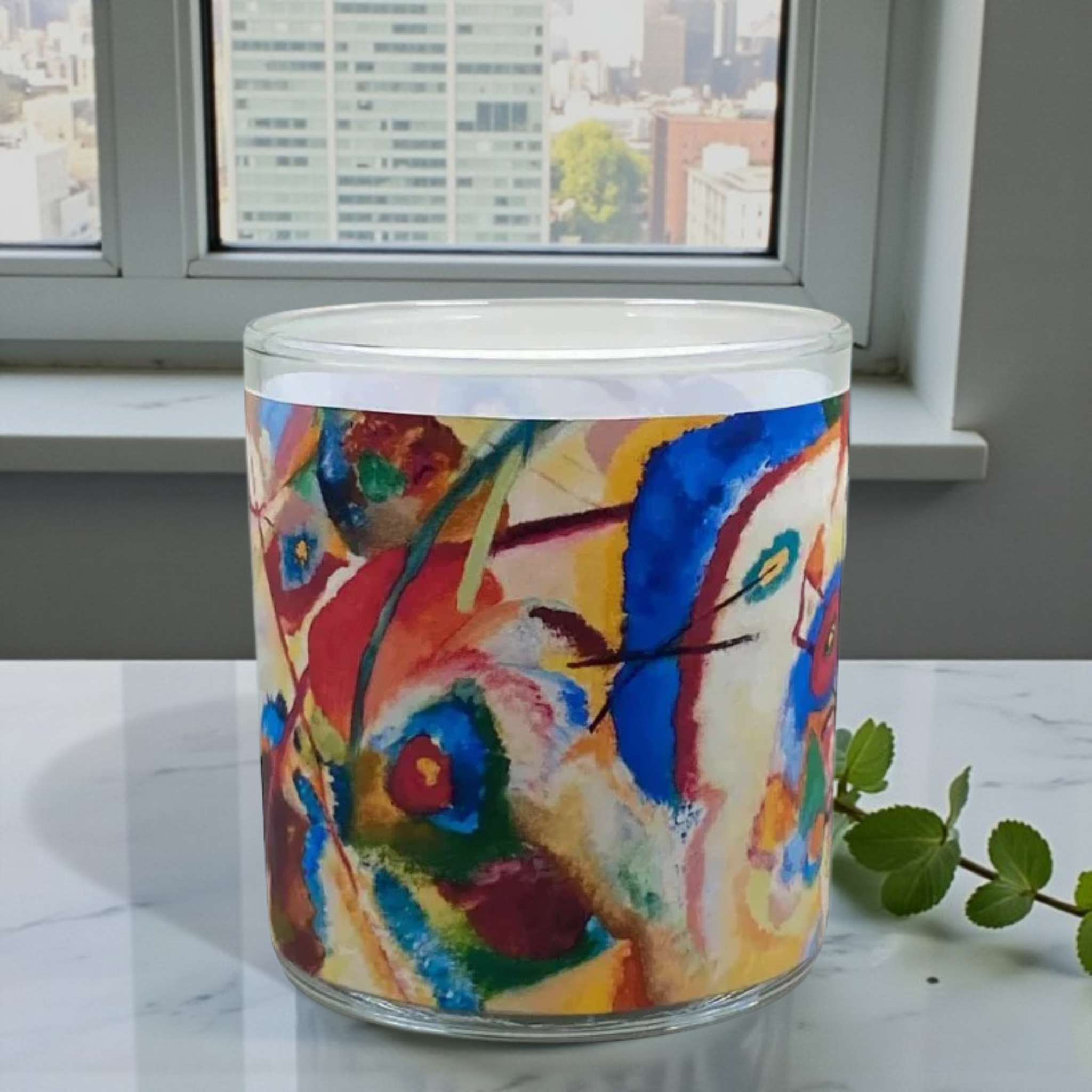 Colorful abstract-patterned candle on a marble surface with a window view in the background
