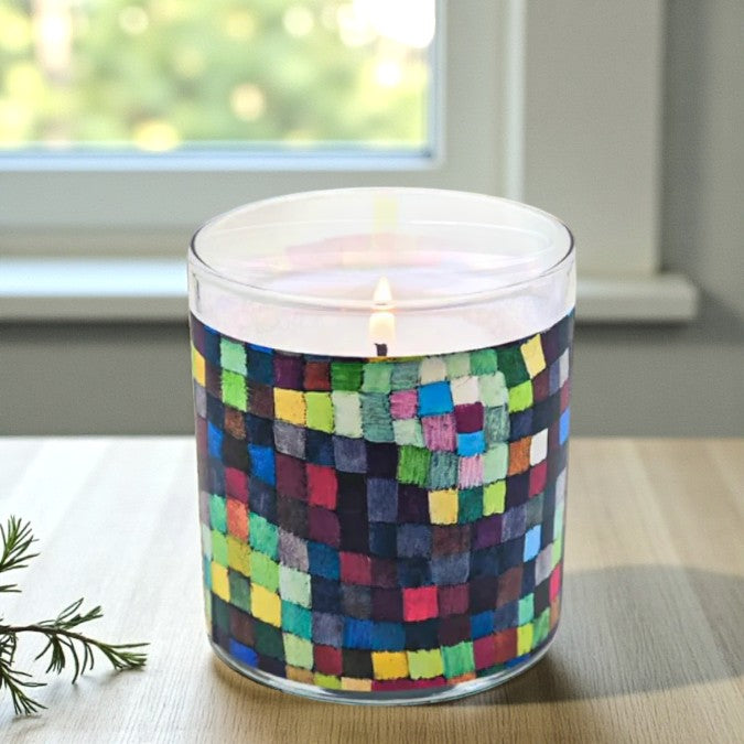 Candle in a glass jar with a colorful checkered pattern on a table.