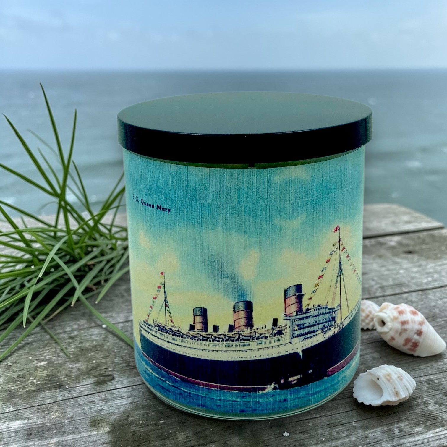 Candle with a ship design on a wooden surface near the ocean