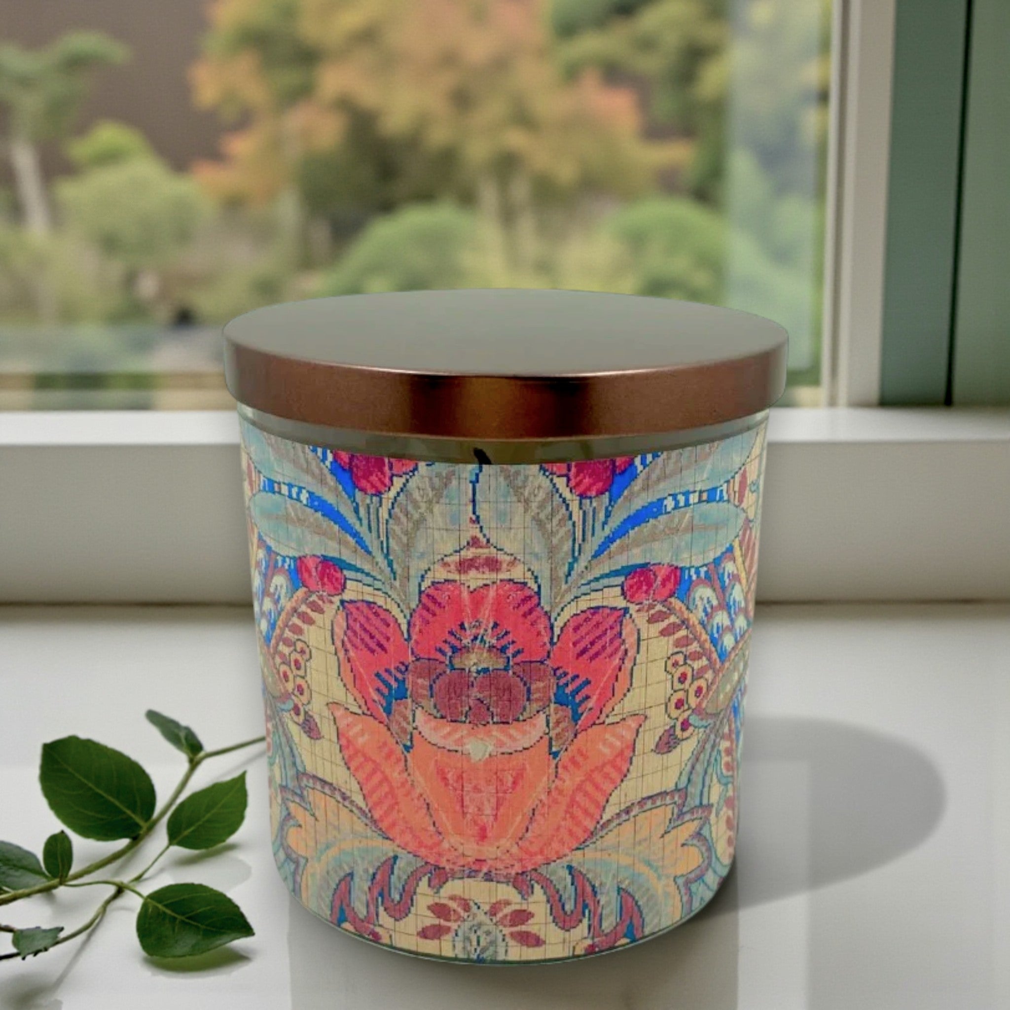 Decorative candle with floral design on a windowsill with greenery
