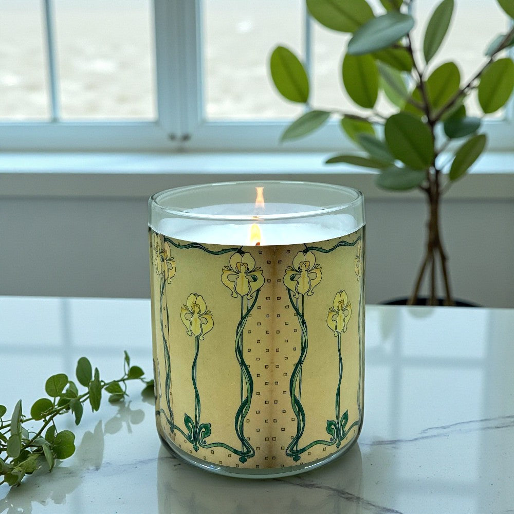 Candle with decorative design on a marble surface with plants in the background