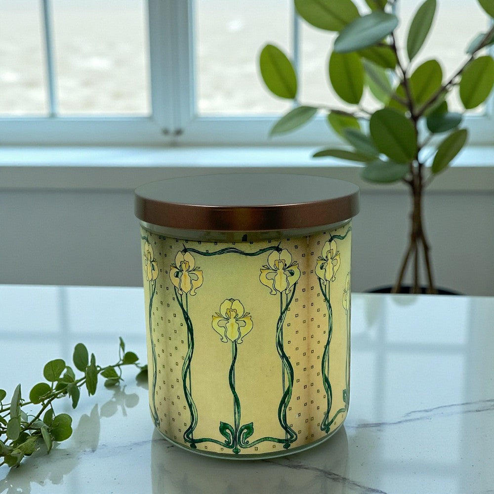 Decorative candle with floral design on a marble surface with a plant in the background