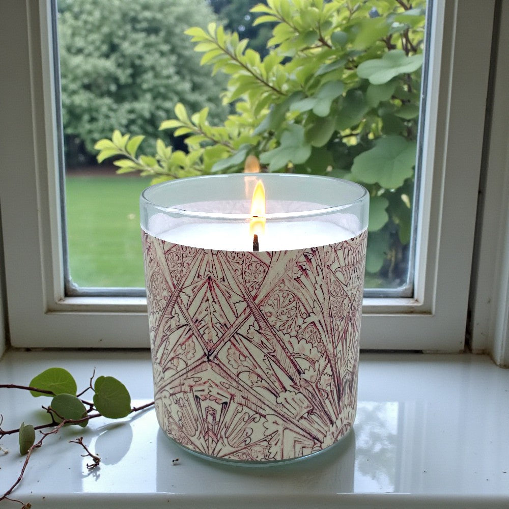 Candle in a patterned container on a windowsill with greenery outside