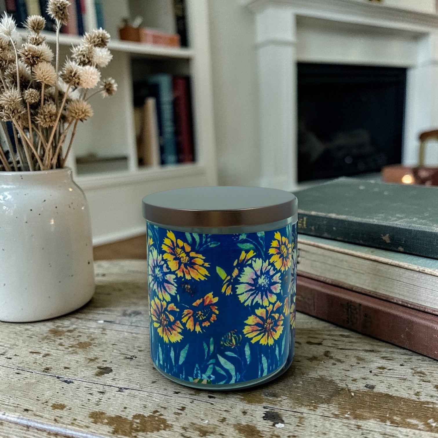 Candle with Frances Gearhart Arts & Crafts era woodblock print floral design on a wooden surface, with a vase of dried flowers and books in the background.