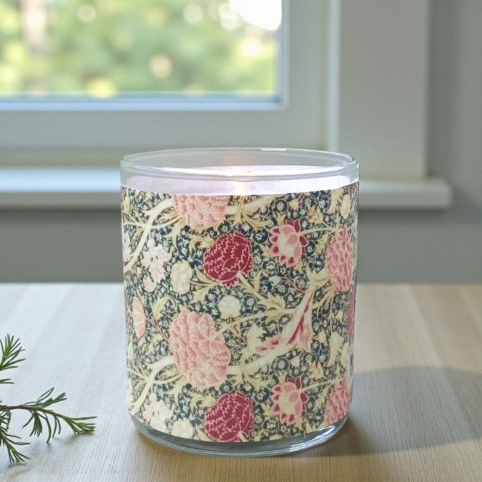 Glass candle with floral pattern on a wooden surface near a window