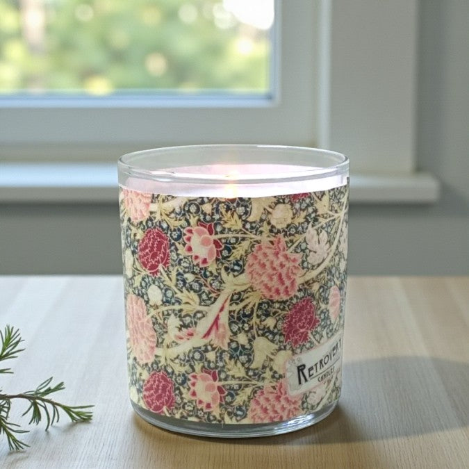 Candle in a floral-patterned jar on a table with a window in the background